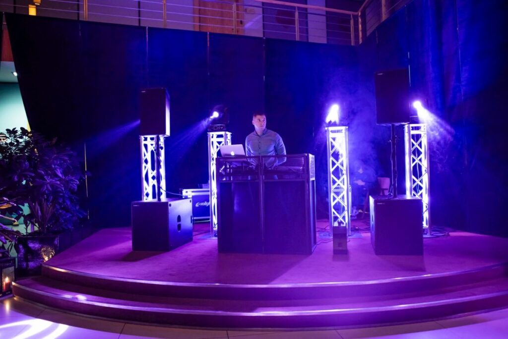 DJ za konsoletą na scenie w niebieskim oświetleniu z konstrukcją truss