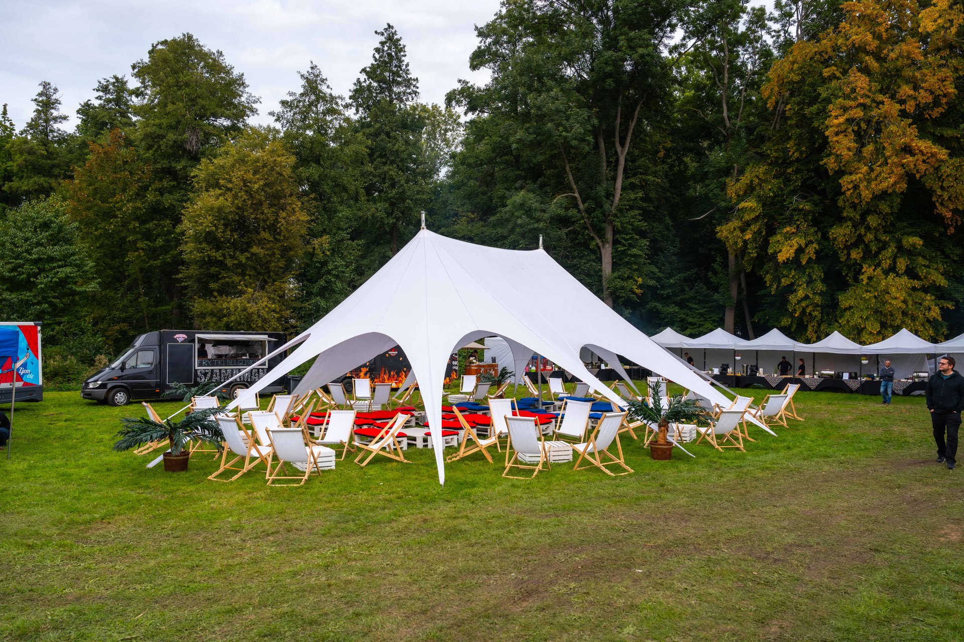 Namiot gwiazda z leżakami wokół paleniska i food truck obok – strefa chillout na pikniku firmowym