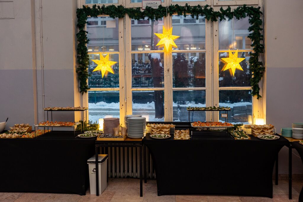 Bufet z zimnymi przekąskami przy oknie z podświetlanymi gwiazdami - catering firmowej wigilii
