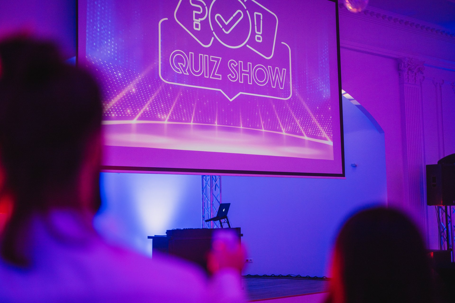 Plansza startowa Quiz Show na ekranie projekcyjnym, przed nim uczestnicy w fioletowym świetle
