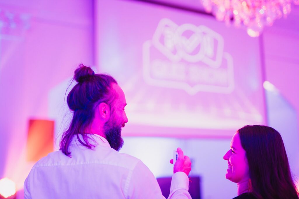 Dwoje uczestników przed ekranem z logo Quiz Show, w dłoni pilot do odpowiedzi