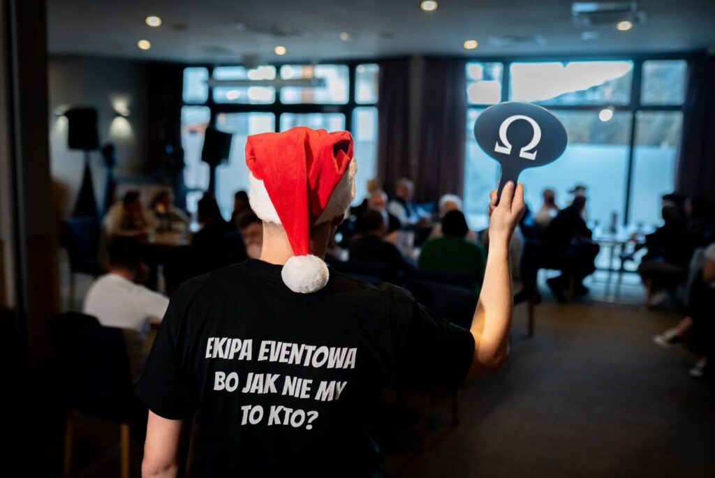 Animatorka w czapce Mikołaja przed salą pełną drużyn podczas świątecznej gry indoorowej