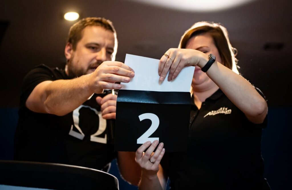 Prowadzący pokazują kopertę z numerem 2 podczas licytacji między rundami gry