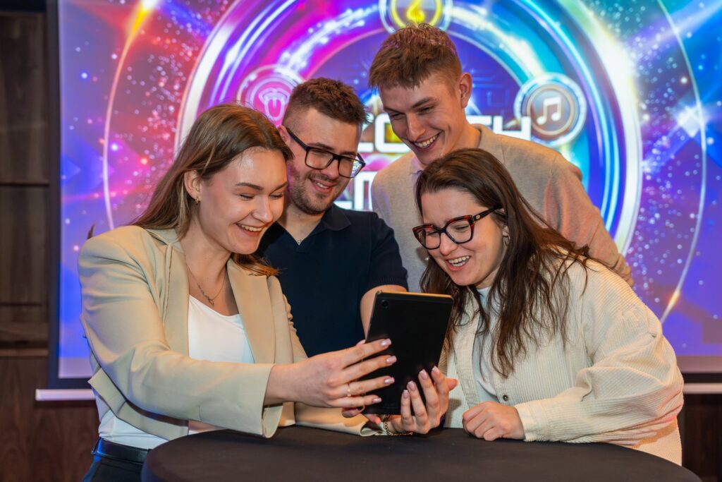 Uśmiechnięta drużyna sprawdza odpowiedź na tablecie przed ekranem teleturnieju