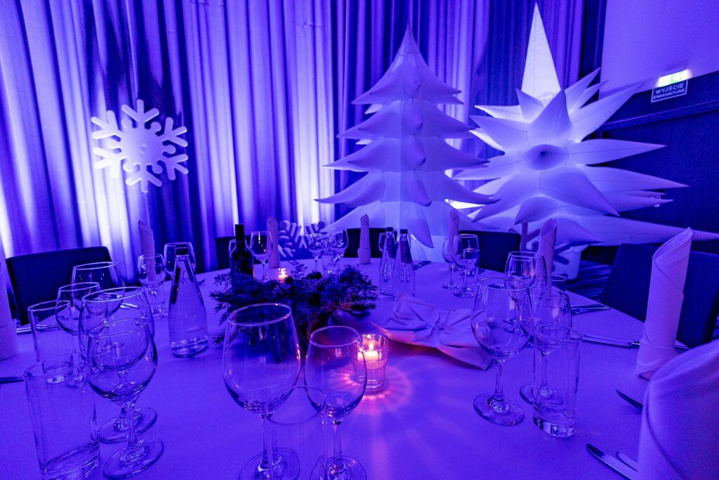 Biała choinka i podświetlana gwiazda nad nakrytym stołem ze świecą i stroikiem - dekoracje Winter Party