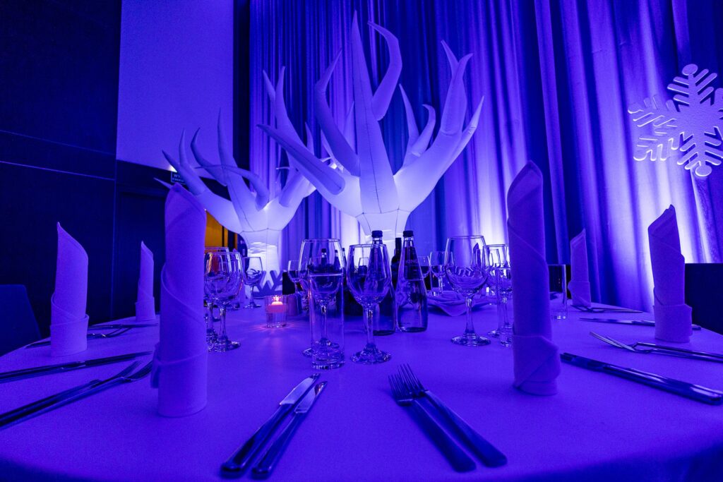 Białe dmuchane drzewa i śnieżynka za stołem z wysokimi serwetkami - zimowa aranżacja sali na Winter Party