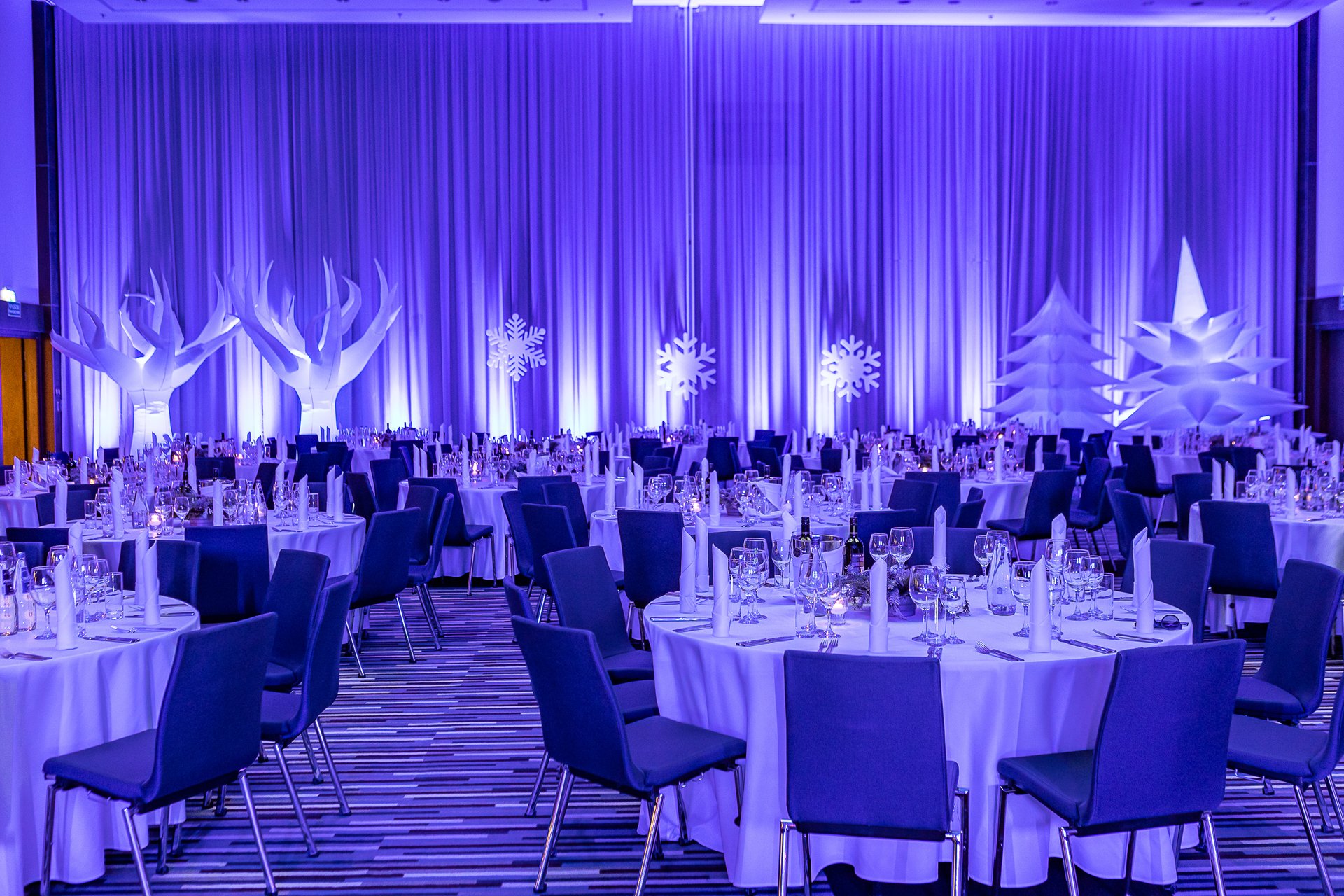 Sala w bieli i fiolecie: białe dmuchane drzewa, podświetlane śnieżynki i choinka-gwiazda za nakrytymi stołami - Winter Party